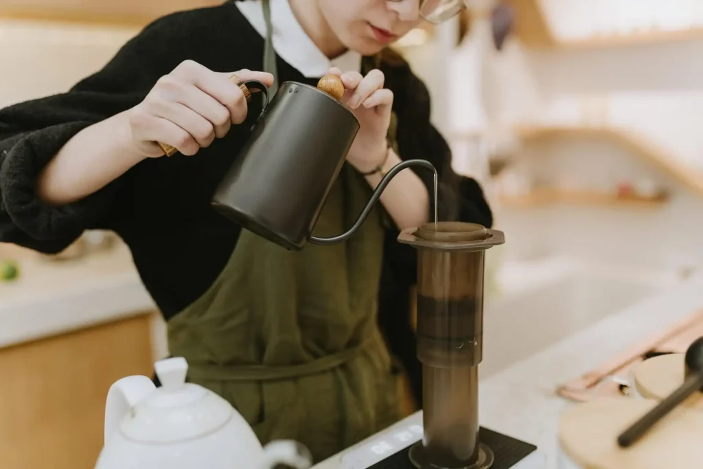 Barista pouring hot water into an AeroPress coffee maker during espresso preparation.