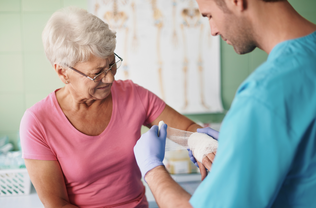 Doctor applying first aid by bandaging elderly woman’s injured hand in a clinic.