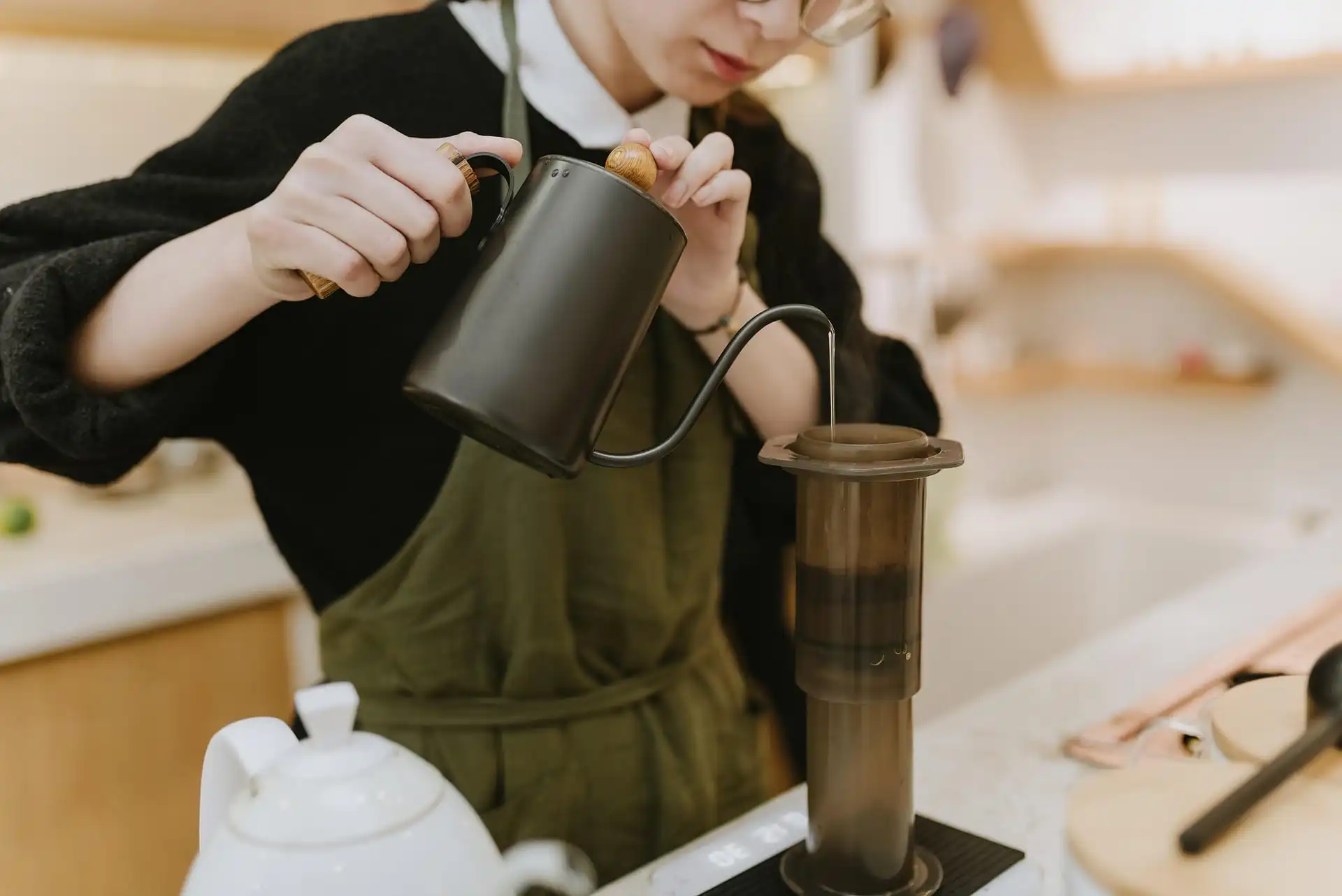 Barista in apron carefully brewing espresso using AeroPress in a café kitchen.